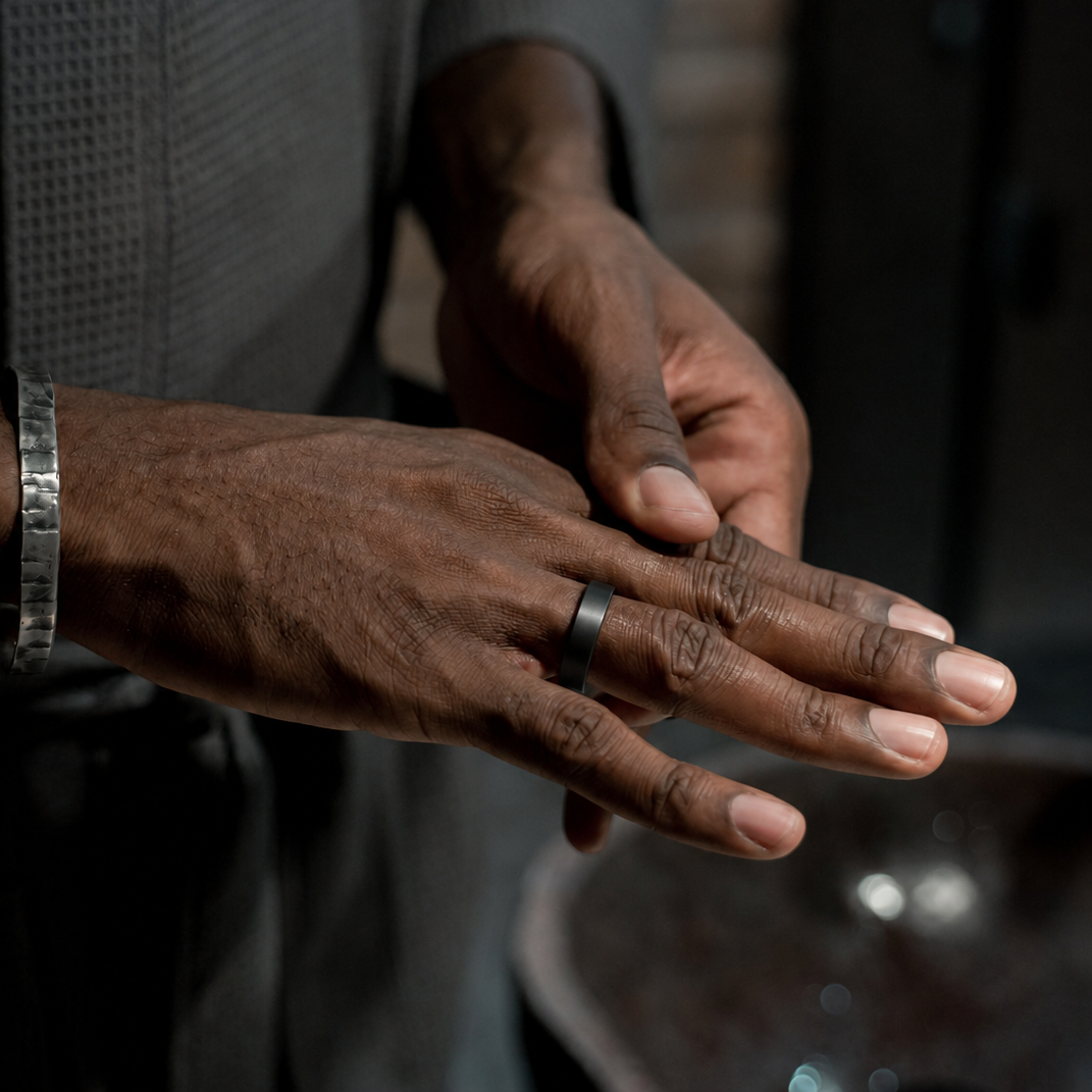 Close-up of an R10 Black Smart Ring worn on a man's finger in a dark indoor setting#color_r10-black