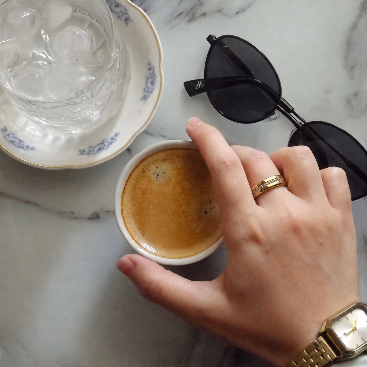 V6 Champagne Gold smart ring worn while holding a coffee cup beside sunglasses on a marble table#color_v6-diamond-gold