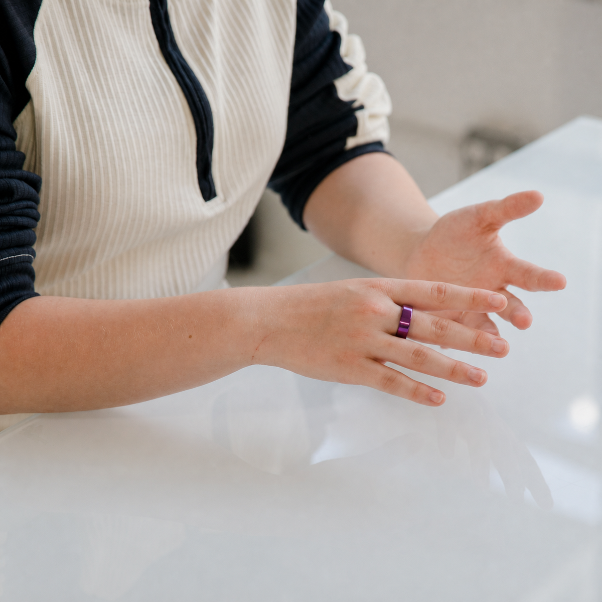 Woman wearing a polished purple smart ring while gesturing at a table#color_purple