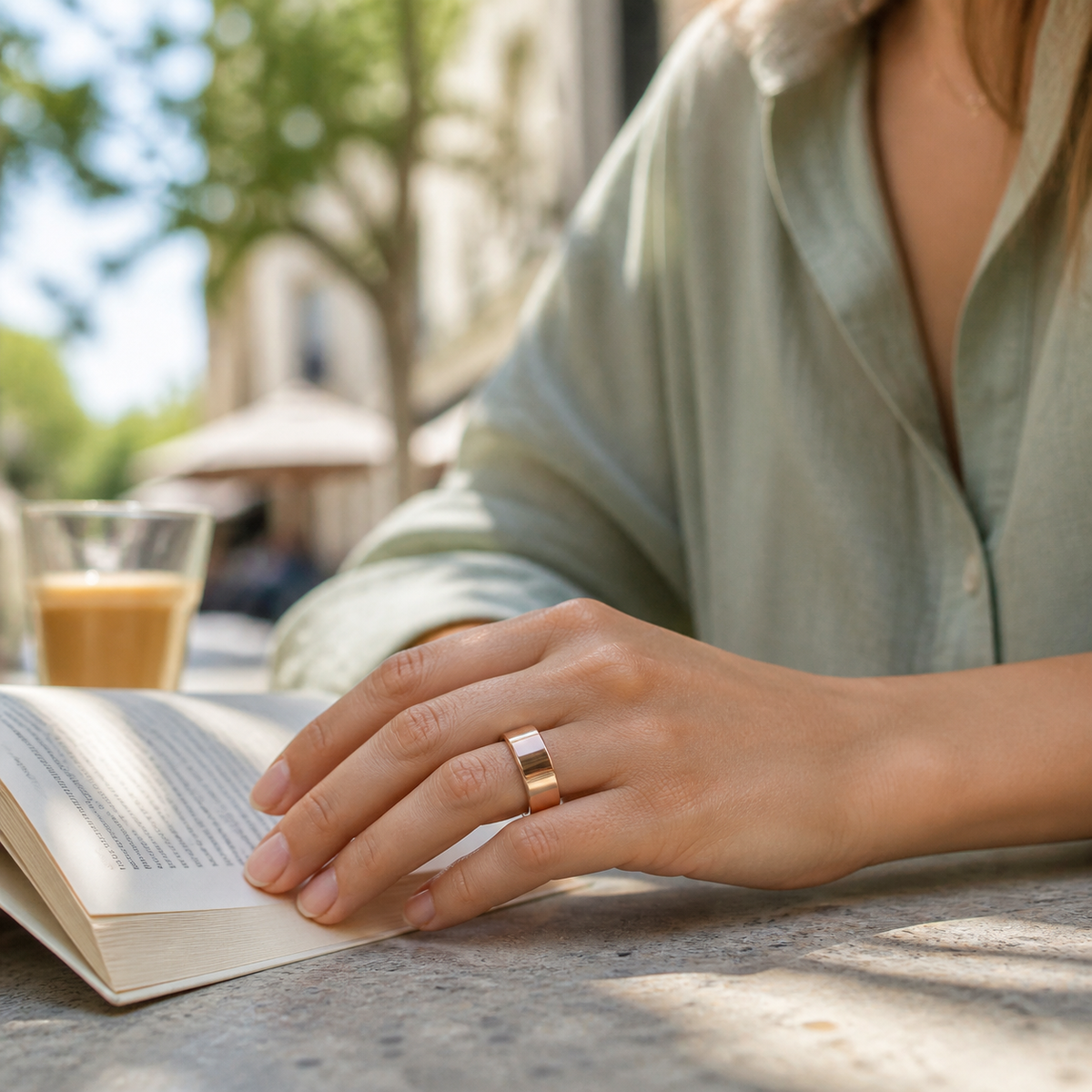 Woman wearing a rose gold SR1 smart ring while reading at an outdoor cafe#color_sr1-rose-gold