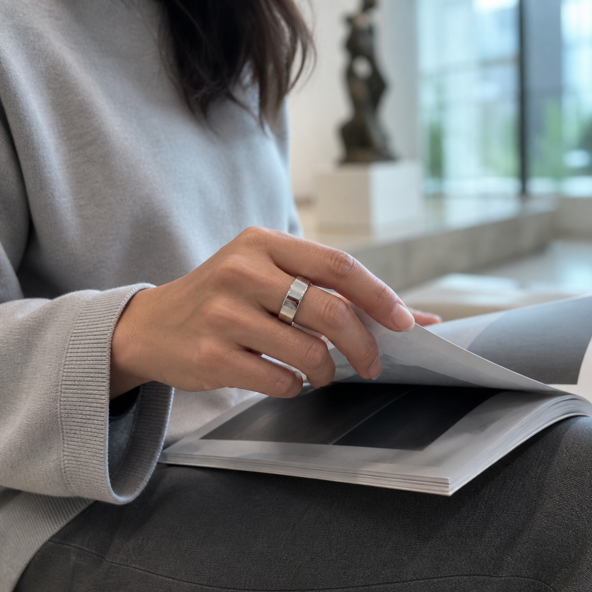 Woman wearing a polished silver SR1 smart ring while reading in a gallery#color_sr1-silver
