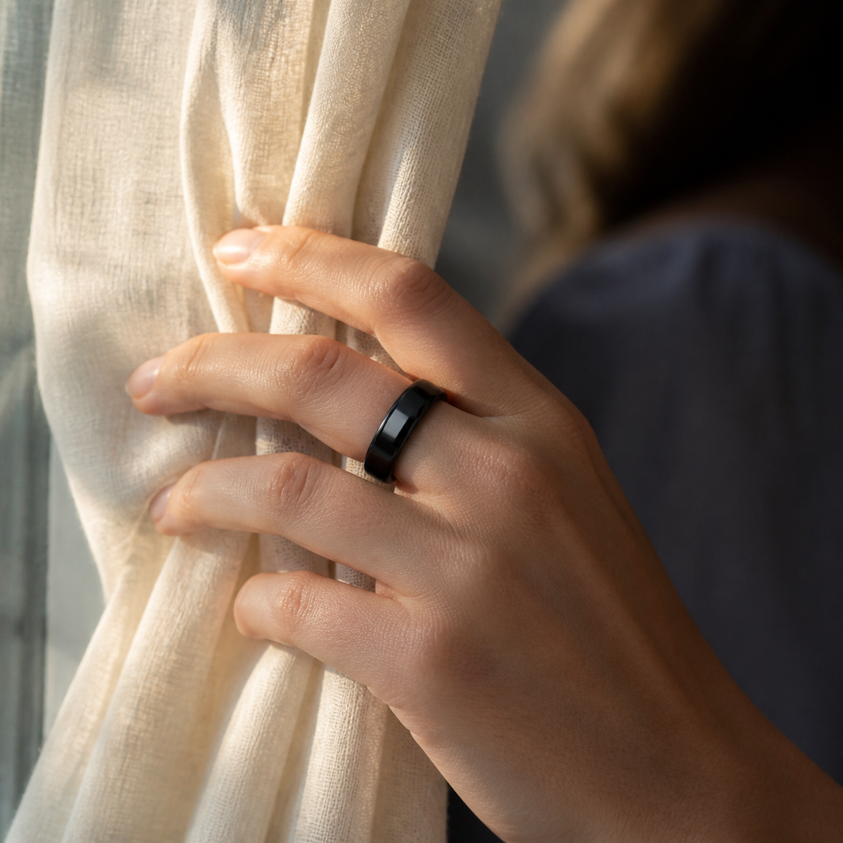 Woman wearing a black ceramic smart ring by a sunlit curtain