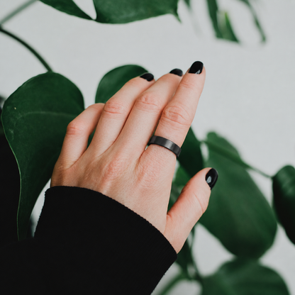 R10 Black Smart Ring worn on a hand against a green plant background#color_r10-black
