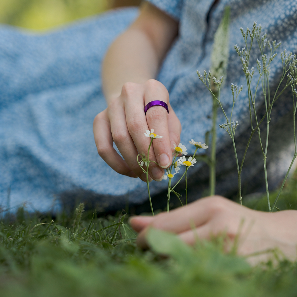 Woman wearing a polished purple smart ring while picking wildflowers#color_purple
