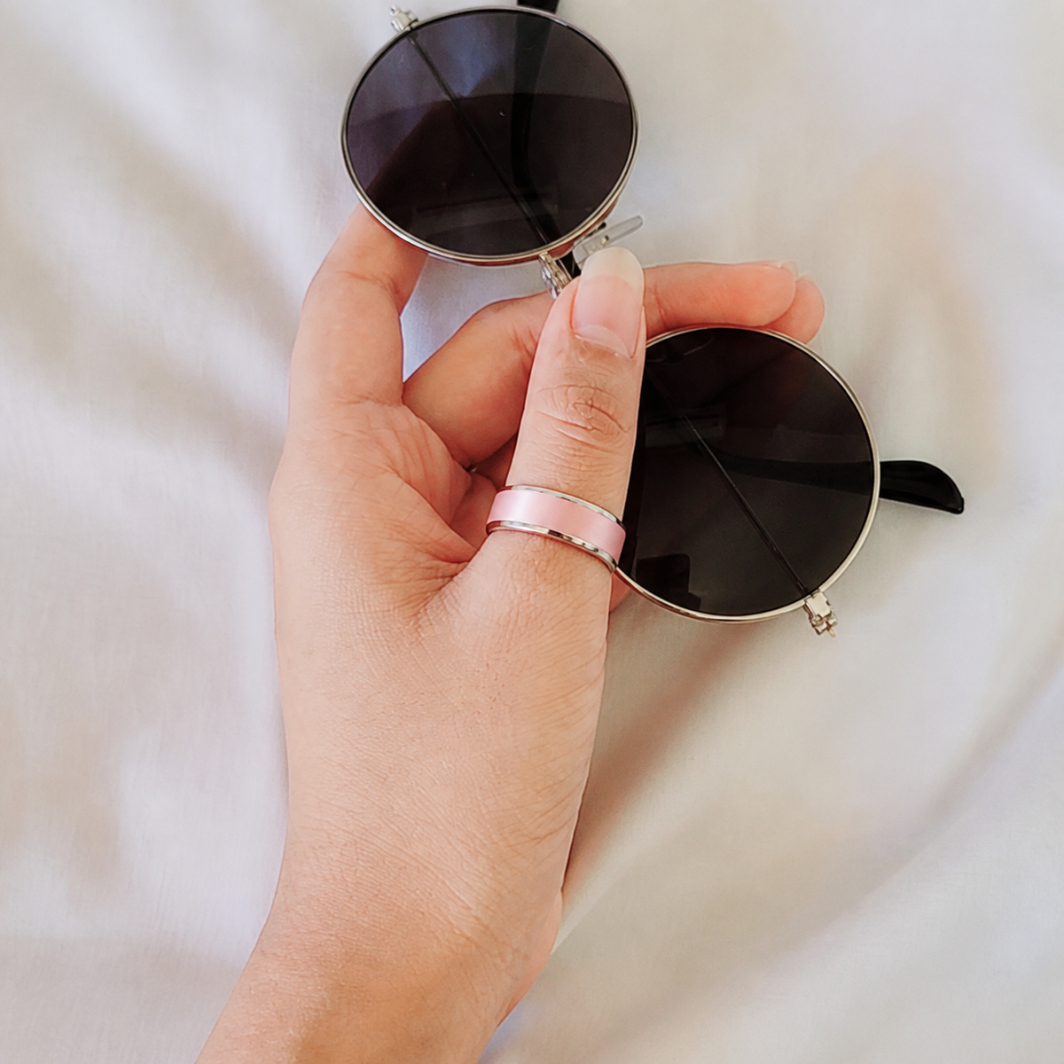 Woman wearing a matte pink R5 smart ring while holding sunglasses#color_r5-pink